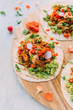 three tortillas with meat, vegetables and sauce on a cutting board next to other food items