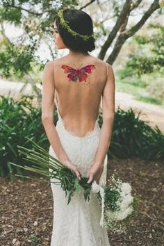 the back of a woman's wedding dress with a butterfly tattoo on her upper back