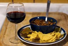 a bowl of chili, tortilla chips and a glass of wine on a tray