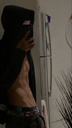 a shirtless man with no shirt on looking at his cell phone in front of the refrigerator