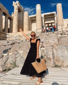 a woman in a black dress is standing on some steps with her hand up to the sky