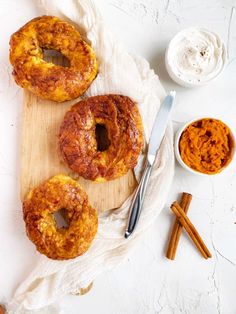 three doughnuts sitting on top of a wooden cutting board next to cinnamon sticks