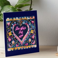 a heart with arabic writing in the middle on a table next to a potted plant