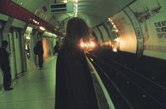 a woman standing in front of a train at a subway station with her back to the camera