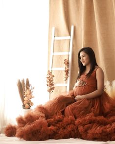 a pregnant woman sitting on top of a bed next to a ladder in an orange dress