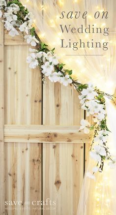 a white wedding lightening with flowers and greenery on the side of a wooden fence