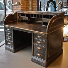 an old fashioned desk with drawers in front of a brick wall and glass doored window