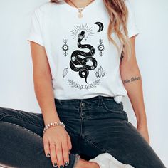 a woman sitting on the ground wearing jeans and a t - shirt with a snake printed on it