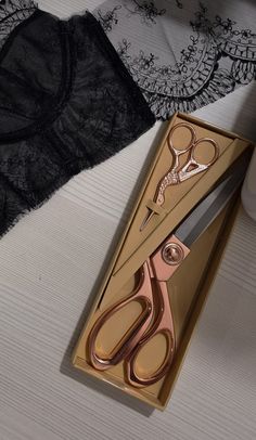 a pair of scissors sitting in a box on top of a bed next to a bra