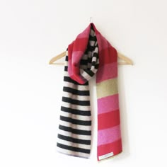 a pink, black and white striped scarf hanging on a wooden hanger against a white wall