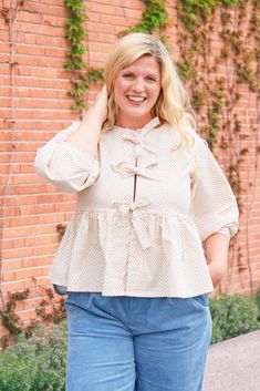 a woman standing in front of a brick wall wearing blue jeans and a white blouse