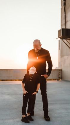 a man standing next to a little boy on top of a cement floor in front of the sun