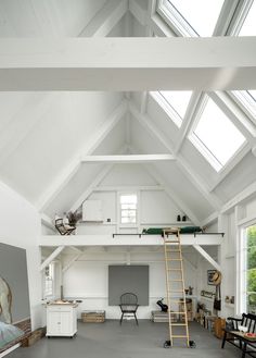 a loft with white walls and high ceilings has a ladder leading up to the loft