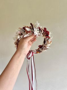 a hand holding a dried flower wreath with ribbon around it's wrist, on a white background