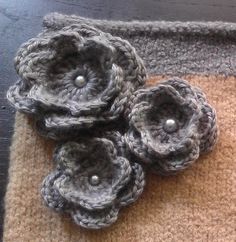 three crocheted flowers sitting on top of a brown and gray mat next to each other