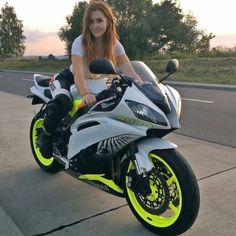 a beautiful young woman sitting on top of a white and yellow motorcycle next to a road