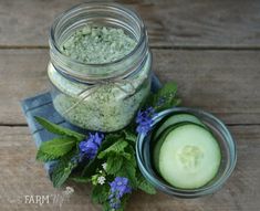 a jar filled with green stuff next to a cucumber on top of a blue towel