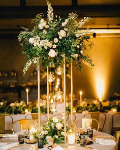 a tall centerpiece with flowers and candles sits on top of a round dining table