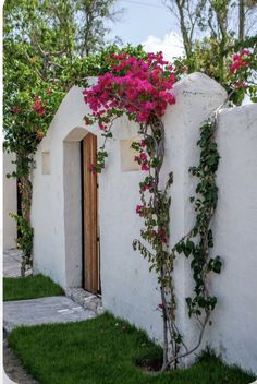 a white building with pink flowers growing on it's side and door in the doorway