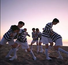 a group of young men standing next to each other on top of a sandy beach