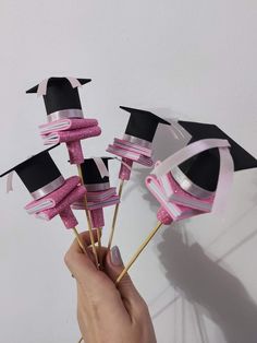 a hand holding some pink and black graduation hats on top of toothpick sticks