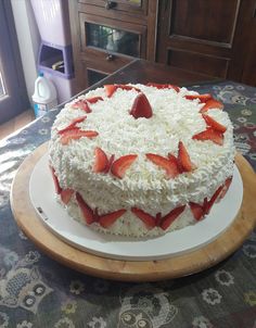 a cake with white frosting and strawberries on top sitting on a wooden platter