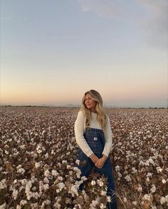 a woman standing in a cotton field with her arms crossed and looking at the camera