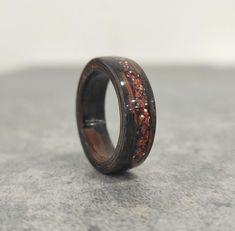 a wooden ring with red and black glitter inlays sits on a stone surface