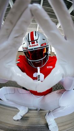 a man wearing a helmet sitting on the ground with his hands up in front of him