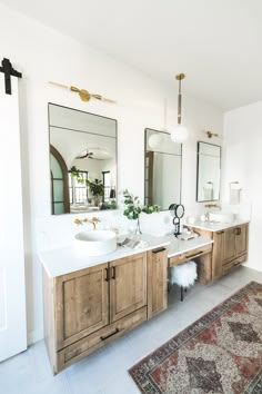 a bathroom with two sinks, mirrors and rugs on the floor in front of them