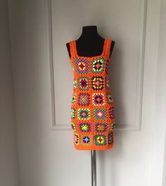 an orange crocheted dress on a mannequin stand in front of a door