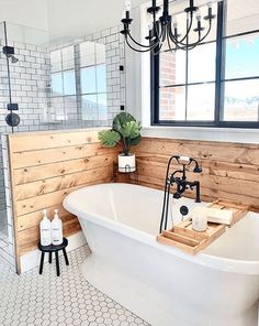 a white bath tub sitting under a window next to a wooden paneled bathroom wall