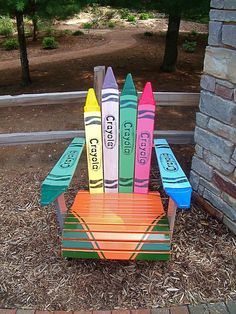 a wooden chair made out of crayons sitting on top of mulch next to a brick wall