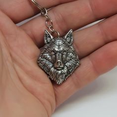 a hand holding a metal keychain with a wolf head on it's face