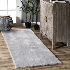 a white rug is on the floor next to a wooden cabinet and potted plant