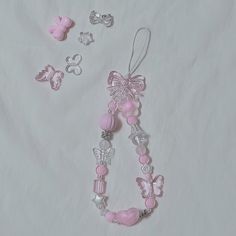 a pink necklace with butterfly charms and other accessories on a white sheeted bed spread