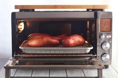 two raw chickens are being cooked in an open toaster oven on a wooden table