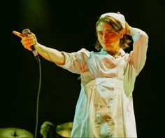 a woman in a white dress holding a microphone and pointing to the side with her right hand