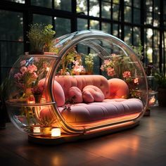 a couch that is sitting inside of a glass case with flowers in it and candles on the floor