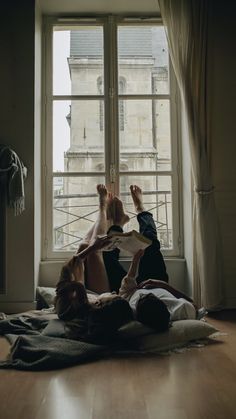 two people are laying on the floor in front of a window with their feet up