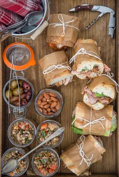 a wooden tray filled with sandwiches and bowls of food next to utensils on a table