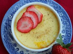 a bowl of pudding with strawberries in it on a blue and white plate next to a strawberry