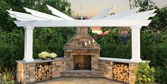 an outdoor fireplace surrounded by white pillars and stone patio furniture with potted plants on either side