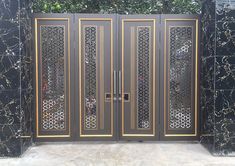 a black and gold gate with intricate carvings on it's sides, in front of a green bush