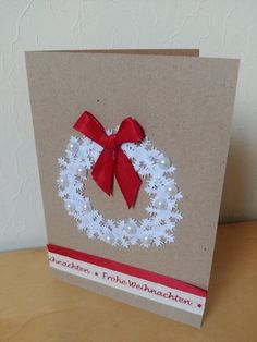 a christmas card with a red ribbon and a white snowflake wreath on it