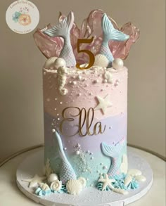 a pink and blue birthday cake with mermaid tail decorations on the top is decorated with seashells