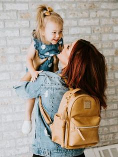 a woman holding a small child in her lap and wearing a backpack on her back