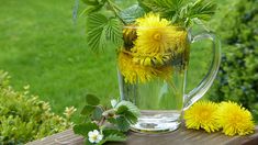 a glass pitcher filled with yellow flowers on top of a wooden table next to green grass