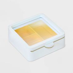 a small white box with a yellow light in the middle on a white surface, it appears to be empty