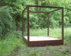 a wooden bed sitting in the middle of a lush green field next to a forest